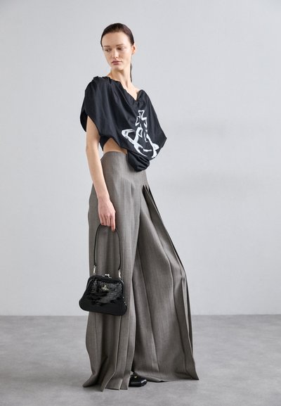 Black oversized top with graphic, gray wide trousers, textured black handbag, and black shoes, set against a neutral background.