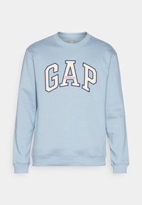 Felpa azzurra chiara in cotone, con un grande logo "GAP" in bianco contornato di blu navy. Polsini e orlo a costine. Design casual.