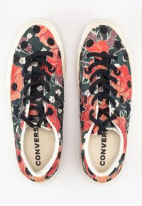 Kwiatowe trampki na płótnie z czarno-czerwono-zielonym wzorem, z czarnymi sznurówkami, białą gumową podeszwą i wyściełaną wkładką.