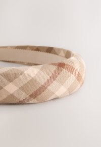 Beige ja ruskea ruudullinen hiuspanta, valmistettu teksturoidusta kankaasta. Siinä on kaareva muoto, sileä sisävuori ja vinoraitakuviot.