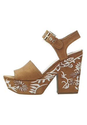 Sandale à plateforme en daim marron avec talon bloc, bride de cheville à boucle, et broderie florale blanche sur le talon et la plateforme.