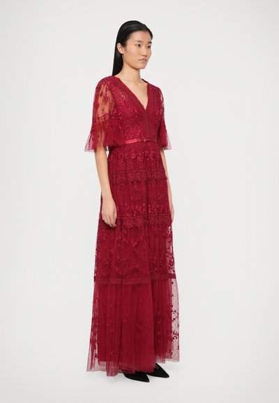 Punane pitsmaksi kleit V-kaelusega, lühikeste läbipaistvate varrukatega, kihilised seelikud ja lilleline tikand. Kombineeritud mustade terava ninaga jalanõudega.