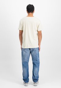 Beige bavlněné tričko s krátkým rukávem, zobrazené z zadní strany. V kombinaci s modrými džíny. Minimalistický design, žádné viditelné vzory.