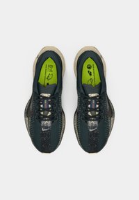 Et par mørkegrønne og beige Nike løbesko med sorte snørebånd, spraglet stribe og lysegrønne indlægssåler på hvid baggrund.