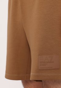 Brune idrettsshorts laget av myk stoff, med en teksturert merkevarelapp på siden og flate sømmer for komfort.
