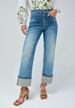 Jeans de tiro alto color azul claro con puños doblados y un acabado desgastado. Combinados con tacones marrones con tiras. La tela parece denim con una ligera textura.