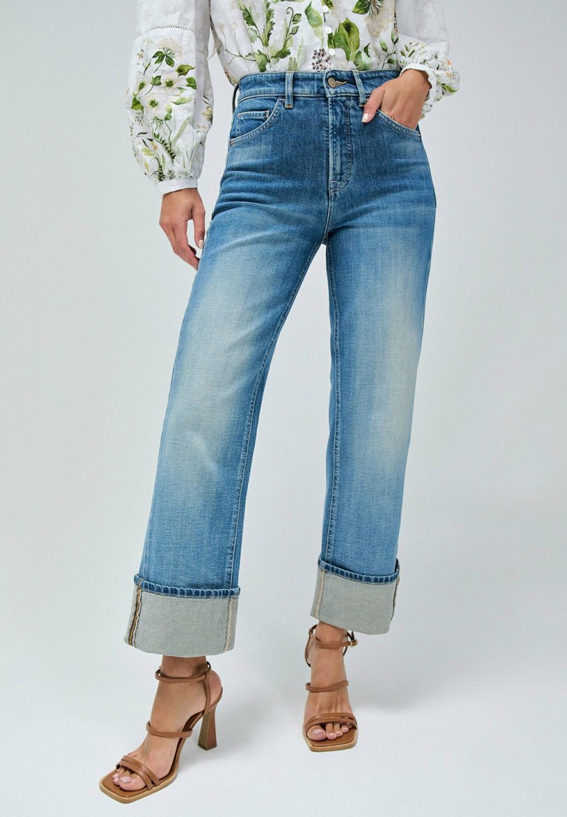 Jeans de tiro alto color azul claro con puños doblados y un acabado desgastado. Combinados con tacones marrones con tiras. La tela parece denim con una ligera textura.
