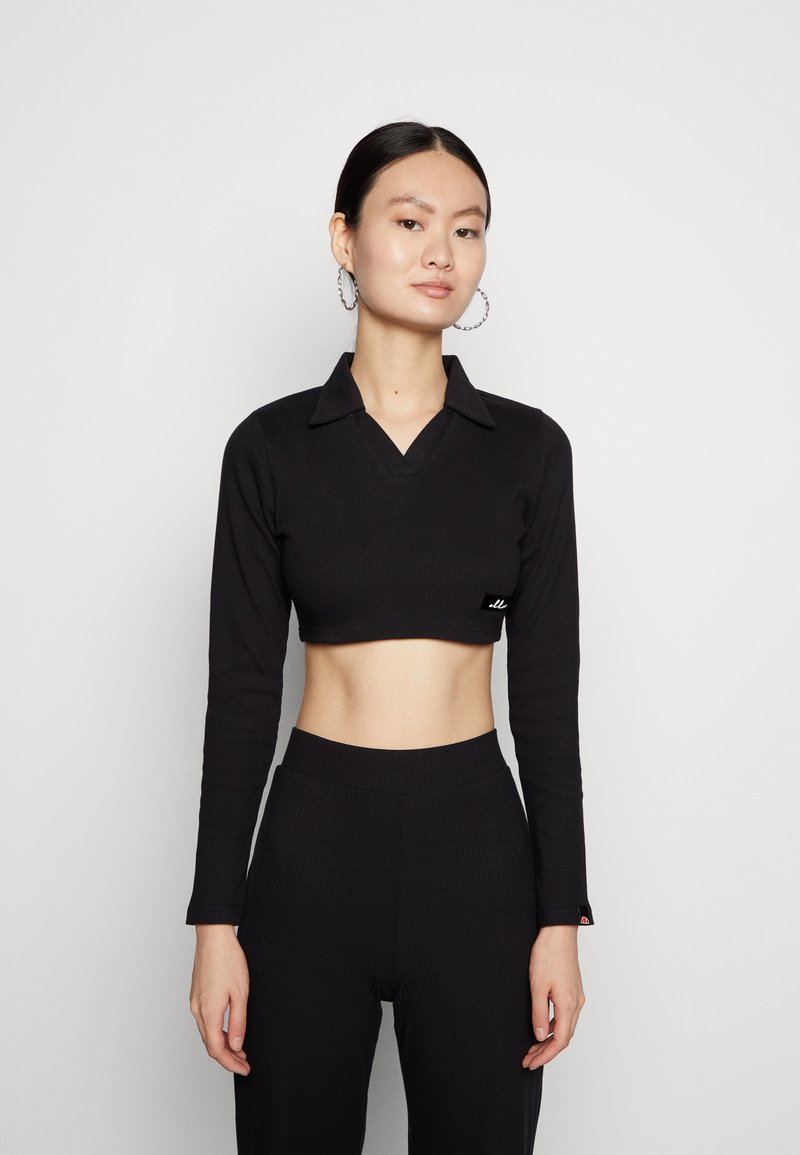 Top preto cropped de mangas longas com decote colarinho, textura canelada e pequeno detalhe da marca perto da bainha. Combinado com calças pretas de cintura alta.