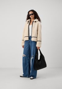 Cream-colored fleece jacket with black trim, paired with blue wide-leg jeans featuring distressed details and a black pleated handbag.
