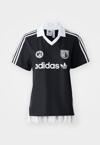 Melns futbols krekls ar baltu apkakli, trīs baltām svītrām uz piedurknēm un logo priekšā. Apakšā ir pleita balta svārku daļa.