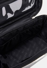 Borsa cosmetica nera con esterno testurizzato, chiusura con zip e interno dotato di sezioni elastiche e motivo a logo. Pannello superiore trasparente.