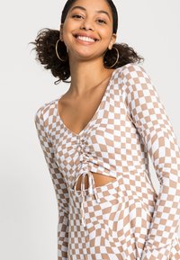 Blusa de mangas longas com um padrão xadrez em bege e branco, com um detalhe franzido na gola e um recorte na lateral.