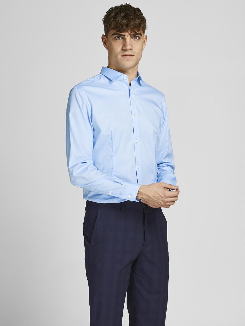 Light blue button-up shirt with a spread collar, long sleeves, and a smooth texture, paired with dark checkered trousers.