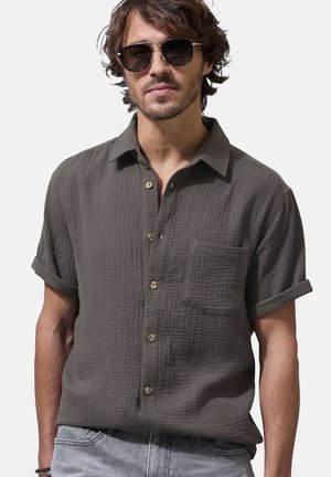 Short-sleeve, dark green button-up shirt made of textured fabric. Features a chest pocket and rolled sleeves, complemented by light buttons.