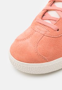 Różowe zamszowe sneakersy z teksturowanym wierzchem, okrągłym noskiem, białą gumową podeszwą i różowymi sznurowadłami. Posiadają detale w postaci przeszyć po bokach.