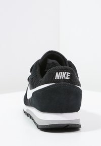 Czarny sportowy but z siateczkowymi i zamszowymi materiałami. Wyróżnia się białym logotypem w kształcie łuku oraz logo na pięcie. Płaska podeszwa z szarymi detalami. Wyświetlony widok z tyłu.