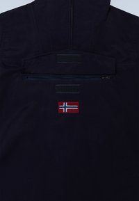 Dark navy jacket back with horizontal zip pocket, Velcro patches above and below, and a small red, white, and blue cross flag patch below the pocket.