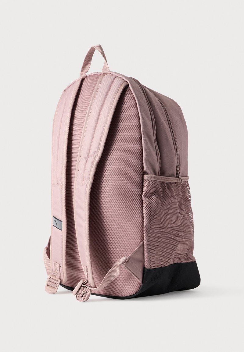 Sac à dos en tissu rose avec bretelles rembourrées, poche latérale en mesh et un accent noir en bas. Comprend deux fermetures éclair à l'avant et une poignée sur le dessus.