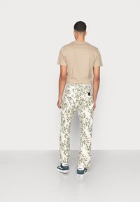 Beige short-sleeve t-shirt paired with white pants featuring a green floral pattern, complemented by navy blue Vans shoes.