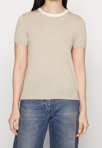 Haut beige à manches courtes avec un col rond, orné d'un bord contrastant de couleur claire, en tissu léger et d'une silhouette ajustée.