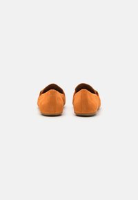 Para pomarańczowych zamszowych loafersów pokazanych od tyłu na białym tle, podkreślających ich minimalistyczny design i detale szycia.