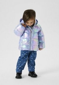 Veste rembourrée irisée avec capuche, dotée d'une fermeture éclair à l'avant et de poignets élastiques, assortie à un pantalon en denim bleu orné de motifs en forme de cœur. Bottes noires.