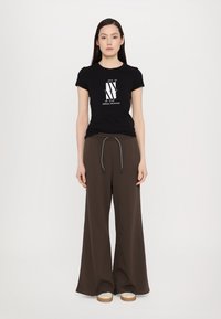 Svart bomull T-skjorte med hvitt Armani Exchange-logo, kombinert med brune vide bukser og beige sko. Enkelt, uformelt antrekk.