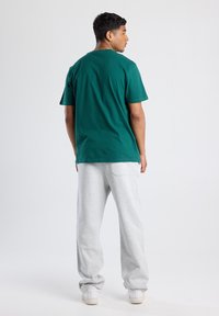 Green cotton t-shirt with a relaxed fit, paired with light gray sweatpants in a soft fabric. The outfit is completed with white sneakers.