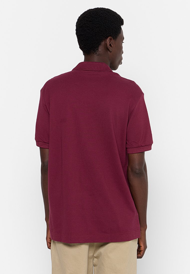Bordowa koszulka polo z teksturowanej tkaniny, krótki rękaw, prążkowany kołnierzyk i prosty dół, noszona z khaki spodniami.