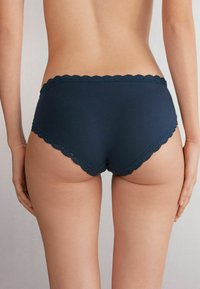 Ropa interior hipster de algodón azul marino con un trim en encaje ondulado a lo largo de la cinturilla, que presenta una textura suave y un diseño de cobertura total.