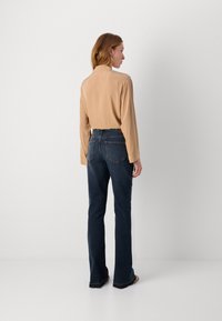 Beige langermet skjorte med samlede skuldre, kombinert med mørkeblå vide jeans. Glatt stoff med en strukturert passform og minimale detaljer.