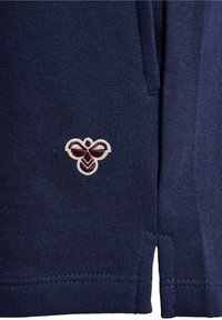 Námorně modrá bavlněná látka s malým vyšitým logem včely v krémové a burgundské barvě, s rovnými lemy a bočními rozparky.