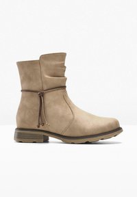 Stivaletto beige con design morbido, realizzato in pelle testurizzata, caratterizzato da una punta arrotondata, lacci marroni e un tacco basso e robusto.