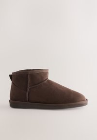 Bottines en daim marron avec un bout arrondi, des détails cousus et une languette à l'arrière. Semelle en caoutchouc plate pour le confort et la stabilité.