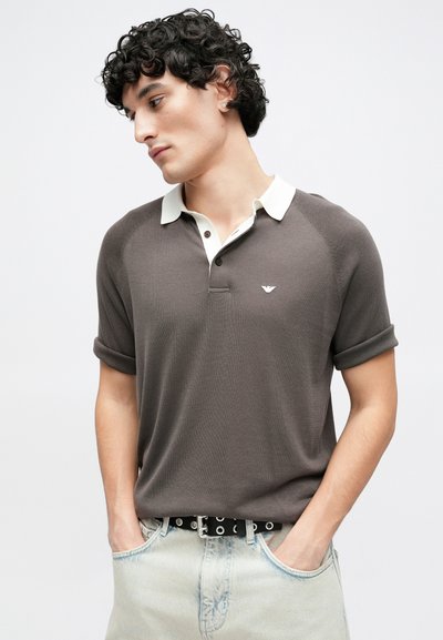 Polo gris foncé avec un col crème, des manches courtes, et un petit logo sur la poitrine gauche, associé à un jean en denim bleu clair.