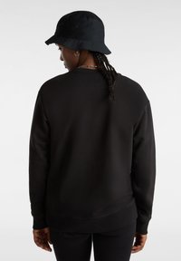 Zwarte sweatshirt met ronde hals en geribbelde boorden, met een zachte textuur. De persoon draagt een zwarte bucket hat.