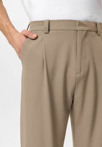 Beige broek met een gladde structuur, een platte voorkant en zijzakken. Voorzien van subtiele plooien en riemlussen in de taille.