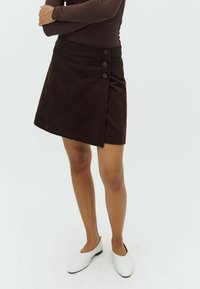 Brun corduroy omslagskirt med en asymmetrisk kant, der har tre knapdetaljer foran og et tekstureret stof.