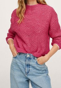 Pull rose tricoté avec un motif ondulé texturé, poignets et encolure côtelés, associé à un jean taille haute bleu clair.