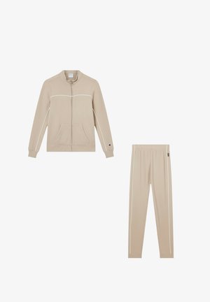 Giacca beige con zip e tasche frontali e pantaloni elasticizzati beige con vita elastica abbinati, entrambi con dettagli di piping bianco.