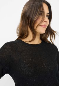 Schwarzer Strickpullover mit Rundhalsausschnitt, versehen mit einem transparenten Material und verstreuten Paillettenakzenten für zusätzliche Details.