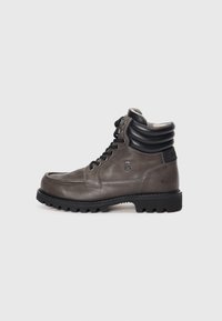 Bottines en cuir gris avec un col rembourré noir, bout rond, semelle extérieure en caoutchouc noir et lacets. Présente un logo en relief sur le côté.