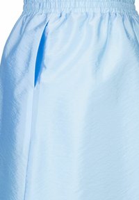 Helles blauer Rock aus glänzendem, leichtem Stoff mit einem elastischen Bund und seitlichen Schlitzen für Bewegungsfreiheit. Glatte Textur.