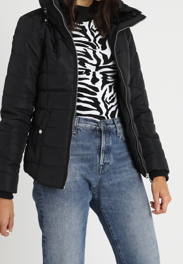 Svart puffjacka med dragkedja, huva och quiltad design. Bärs över en svart och vit zebramönstrad topp och blå denimjeans.