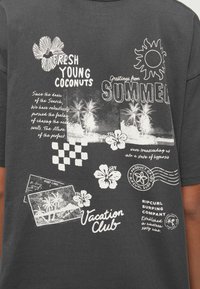 Mustriline musta puuvillane T-särk, millel on valged graafilised trikid troopilistest teemadest, tekst ja ruuduline muster, mis viitab ranna inspiratsioonile.