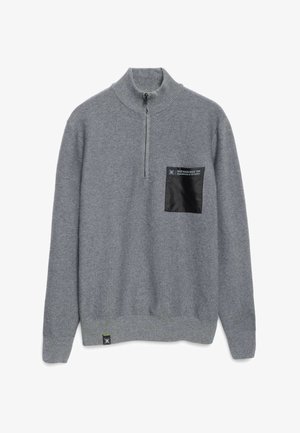 Maglione grigio con colletto alto, zip frontale, tessuto testurizzato e una tasca a toppa nera con testo bianco. Dettagli sul bordo.