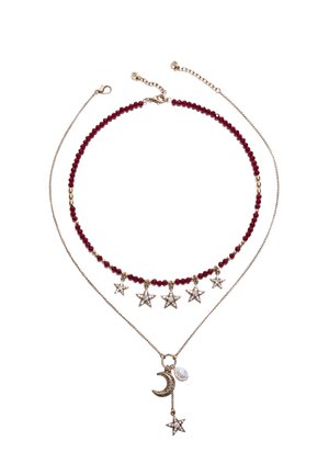 Deux colliers superposés : un avec des perles rouges et cinq breloques étoiles dorées, l'autre chaîne en or avec pendentifs croissant de lune, perle et étoile.