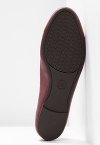 Chaussure en cuir bourgogne avec une surface lisse et une semelle en caoutchouc noir texturée arborant un motif de logo et un design à bout arrondi.