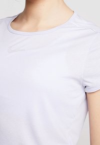 Ljuslila tränings-T-shirt med korta ärmar, rund halsringning och subtil struktur. Har en liten, grå Nike-logotyp på bröstet.