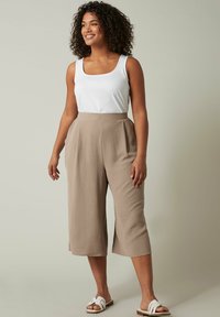 Beige, wijde culottes van textuurstof met hoge taille en zijsplitten, gecombineerd met een witte, aangesloten tanktop en witte sandalen.